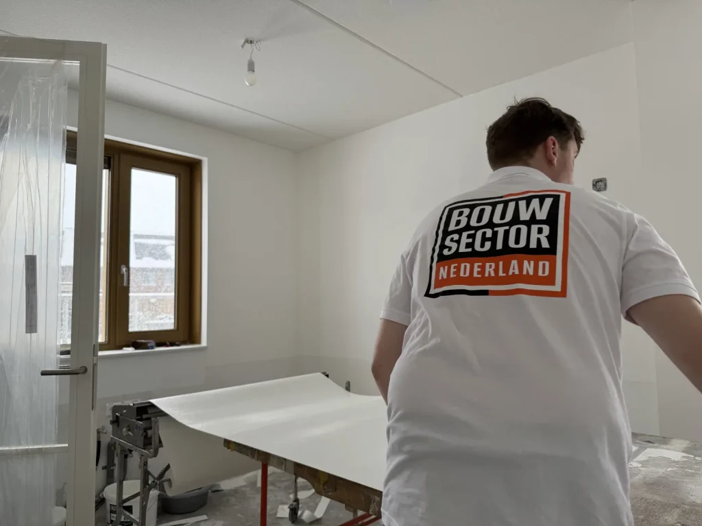 Behanger van Bouwsector Nederland bij de plaktafel met een baan vlies in een kamer met afgeplakte deur