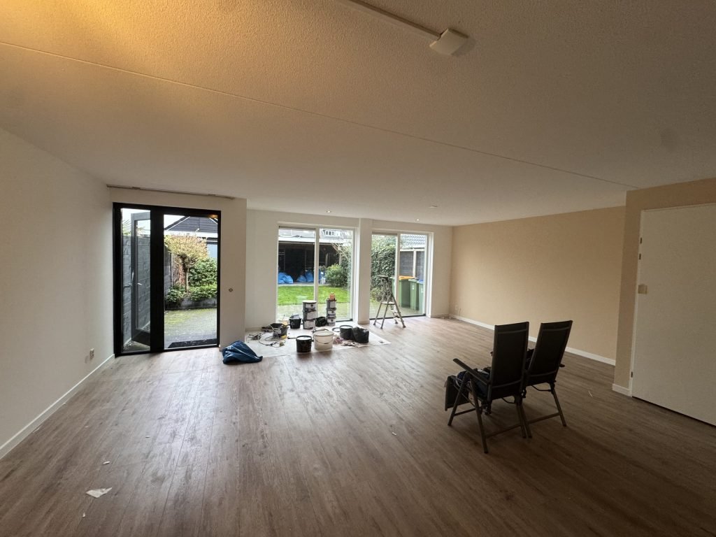 Lege woonkamer met tuindeuren, een trapje en verfemmers klaar voor de behanger