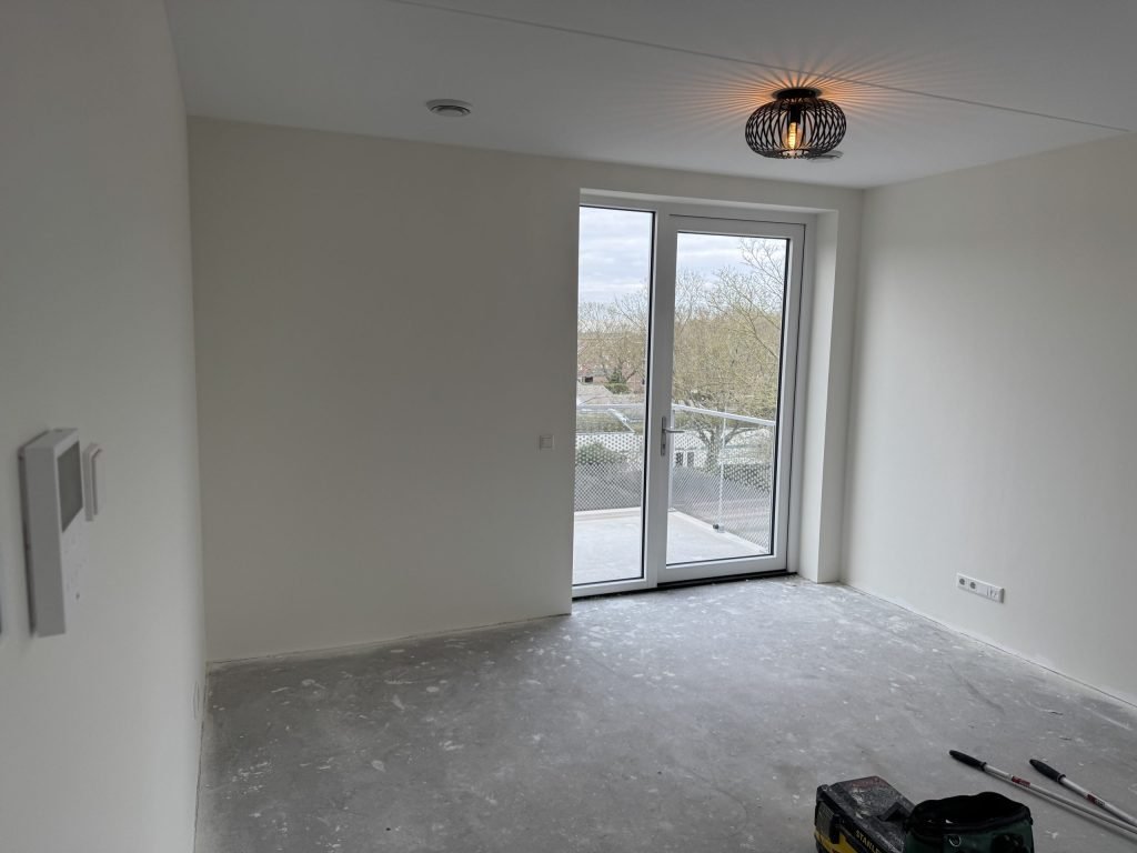 Lege kamer in een nieuw appartement met glazen balkondeur, strakke witte wanden en een betonvloer